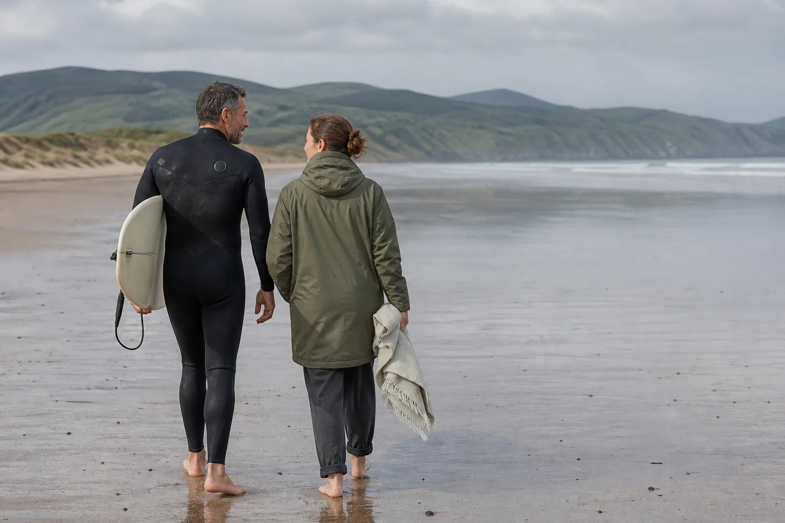 Una pareja camina por la playa después de una sesión; solo una persona lleva tabla.